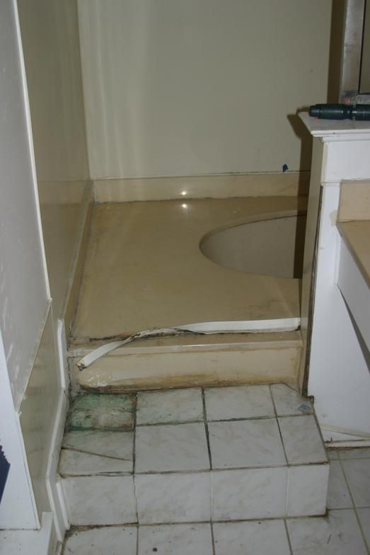 Damaged bathroom with a tiled step leading to a toilet. The tile is cracked, and the surrounding walls are beige.