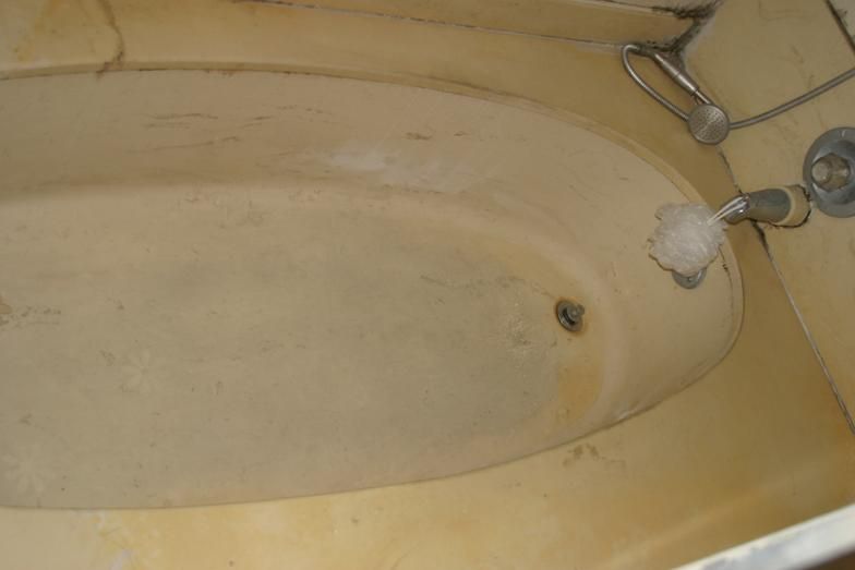 Dirty, stained off-white bathtub with yellow discoloration and fixtures visible.