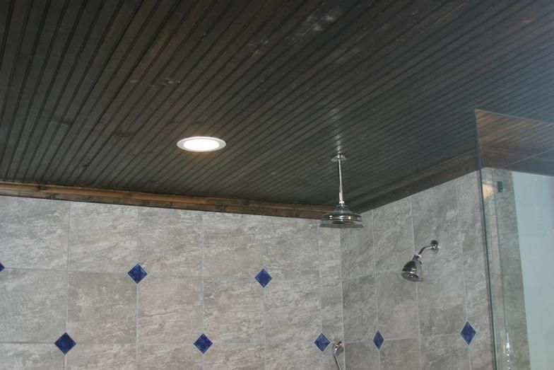 Shower with gray tile, wooden ceiling, and overhead showerhead.