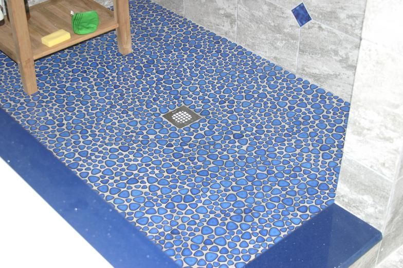 Blue pebble tile shower floor with dark blue edging, built-in bench, and stainless steel drain.