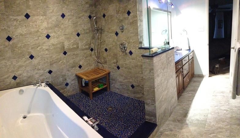 Bathroom with tub and shower. Gray tile walls with blue diamond accents, blue pebble shower floor, brown vanity.