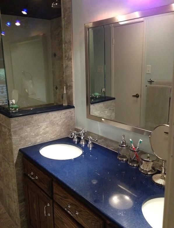 Bathroom with blue countertop, two sinks, large mirror, and brown cabinets.