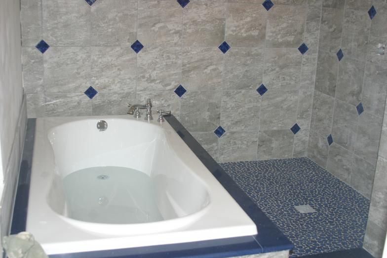 Bathroom with white bathtub, blue tile accents, and pebble shower floor.