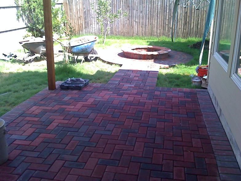 Brick patio leading to a fire pit in a grassy backyard.