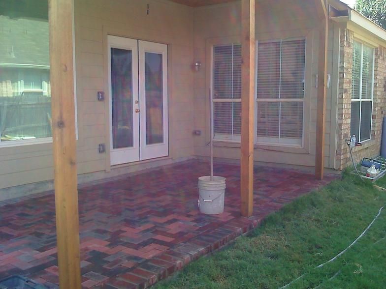 Patio with brick flooring under a covered porch. A white bucket sits on the patio.