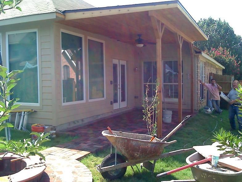 Backyard patio with red brick, wooden pergola, and people working.