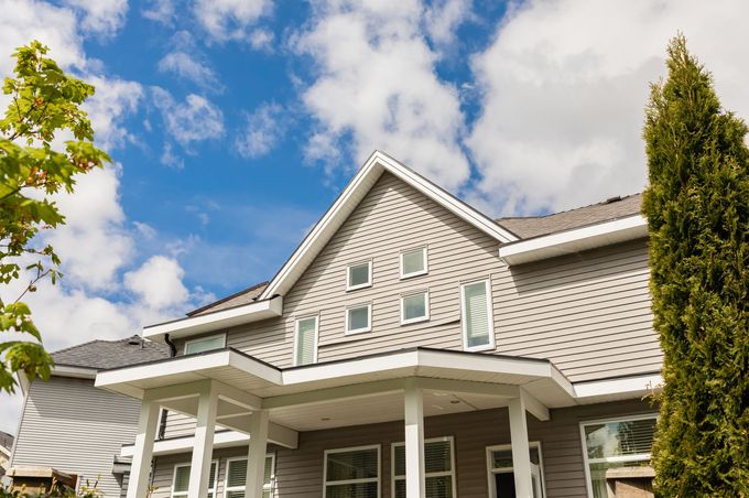 Gray house with white trim, porch, and a blue sky with clouds.