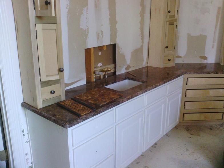 Granite countertop in a kitchen during renovation with white cabinets and unfinished walls.