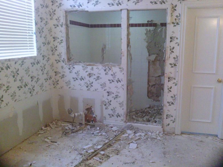 Bathroom under renovation with demolition debris, torn wallpaper, and doorway.