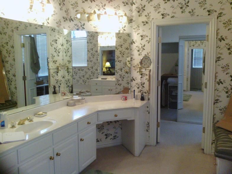 Bathroom with floral wallpaper, white vanity with sink, and open doorway to bedroom.