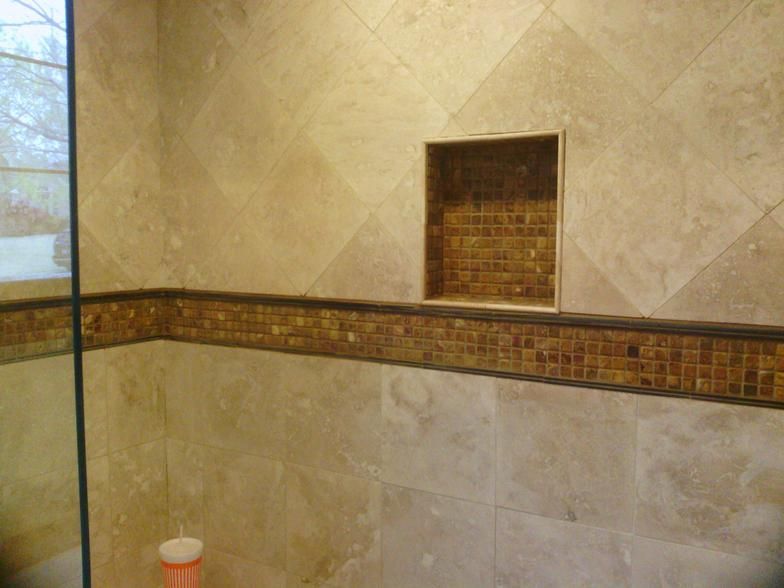 Shower with beige tiled walls, a mosaic tile border, and a built-in shelf.