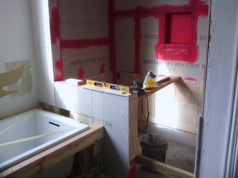 Bathroom under construction: walls with pink waterproofing, tub, and wooden supports.