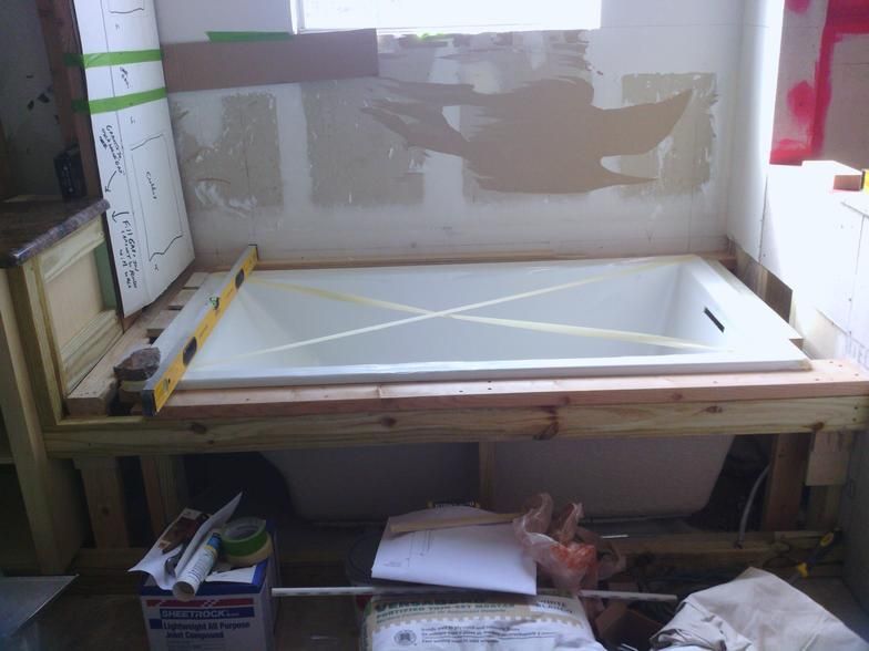 Bathroom renovation in progress: a bathtub framed by wood, surrounded by exposed wall and construction materials.