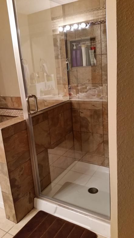 Shower with glass doors and tile walls, a white base, and a brown rug.