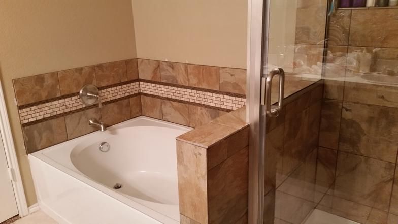 Bathroom with a white bathtub, glass shower door, and brown tile accents.