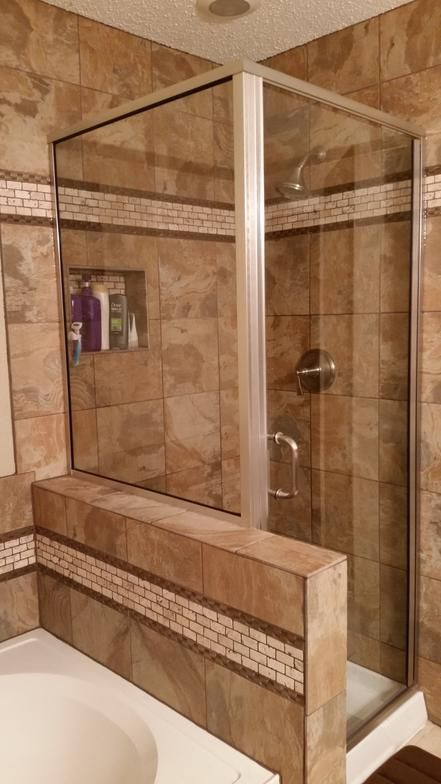 Glass shower enclosure with brown tile walls and mosaic accent.