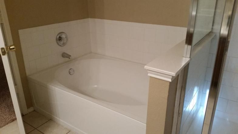 A white bathtub, installed in a bathroom, with a glass shower door.