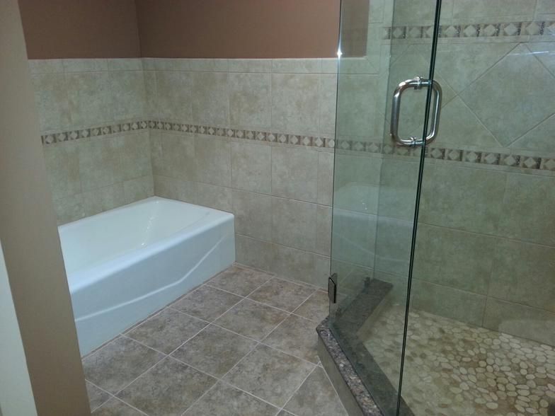 Bathroom with a white bathtub and glass shower door, beige tiles, and brown walls.