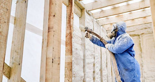 Insulation installer applying spray foam to open framing.