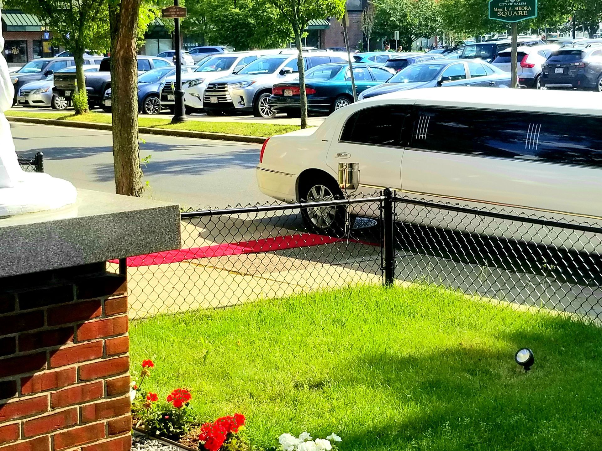 A white limousine is parked in a parking lot behind a chain link fence.