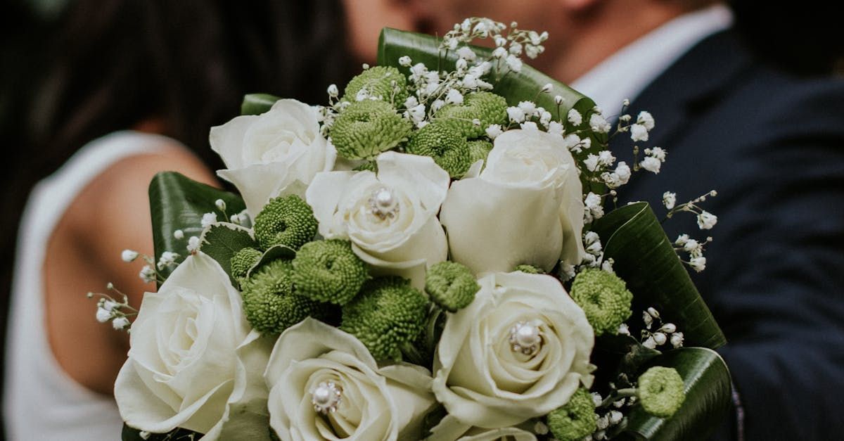 A bride and groom are kissing while holding a bouquet of white roses.