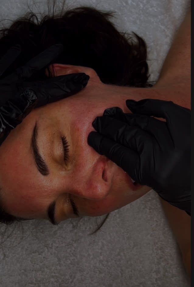 A woman is getting a facial treatment with black gloves on her face.