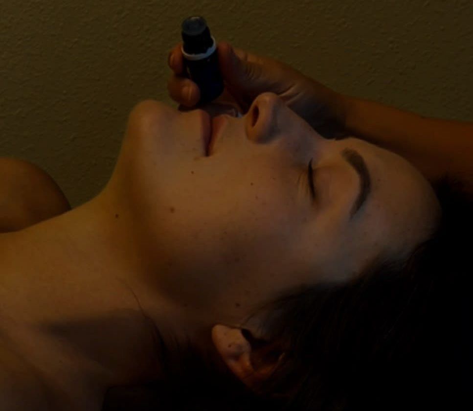 A woman is laying down with her eyes closed and a person is holding a bottle in her mouth.