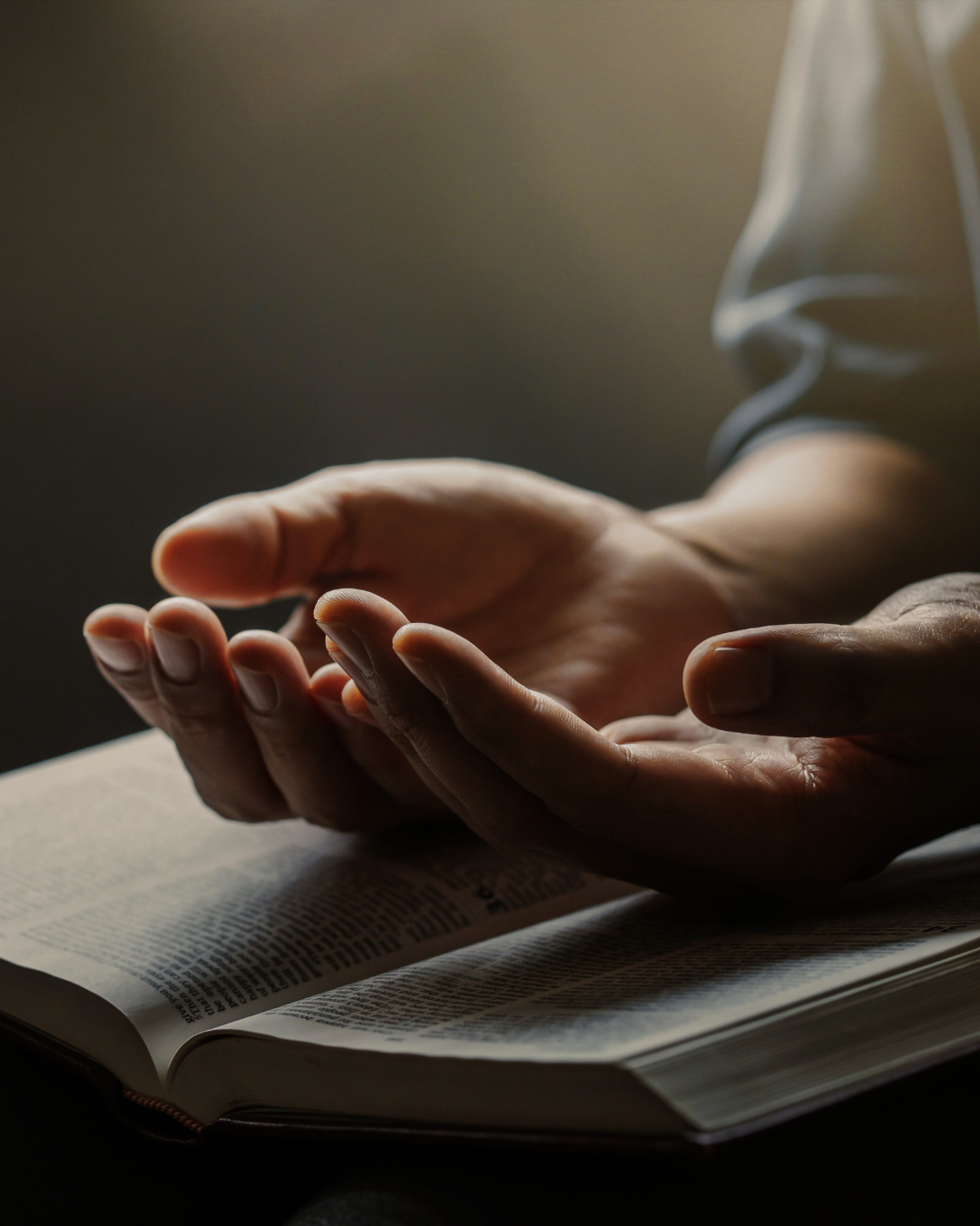 A person is praying over a bible with their hands outstretched.