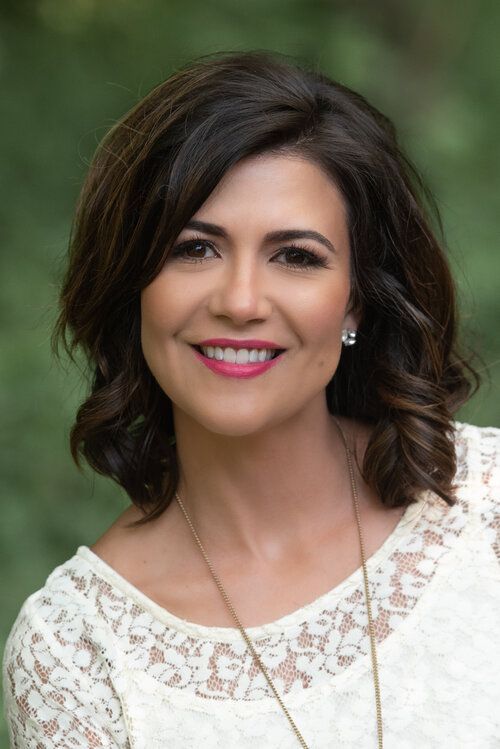 A woman in a white lace top and necklace is smiling for the camera.