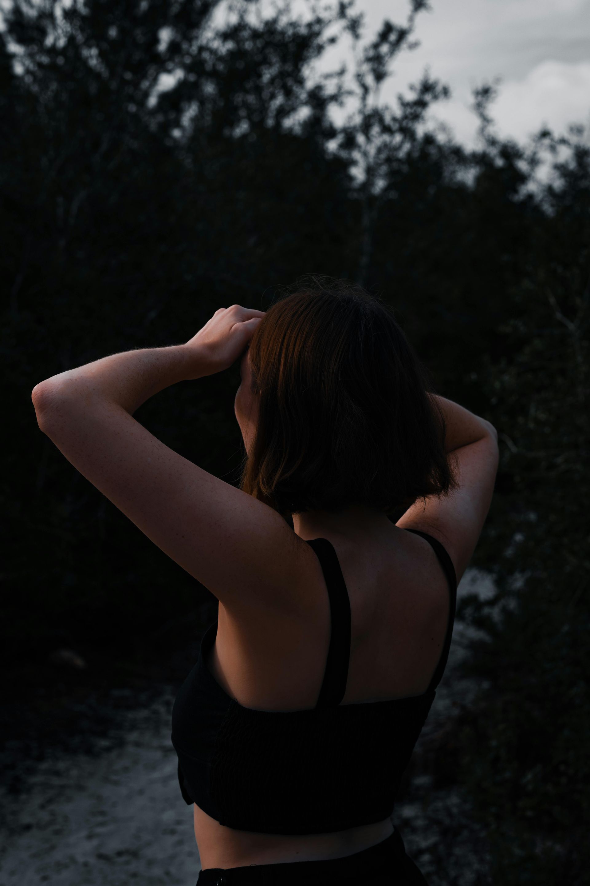 A woman in a black bra is standing in a dark forest.