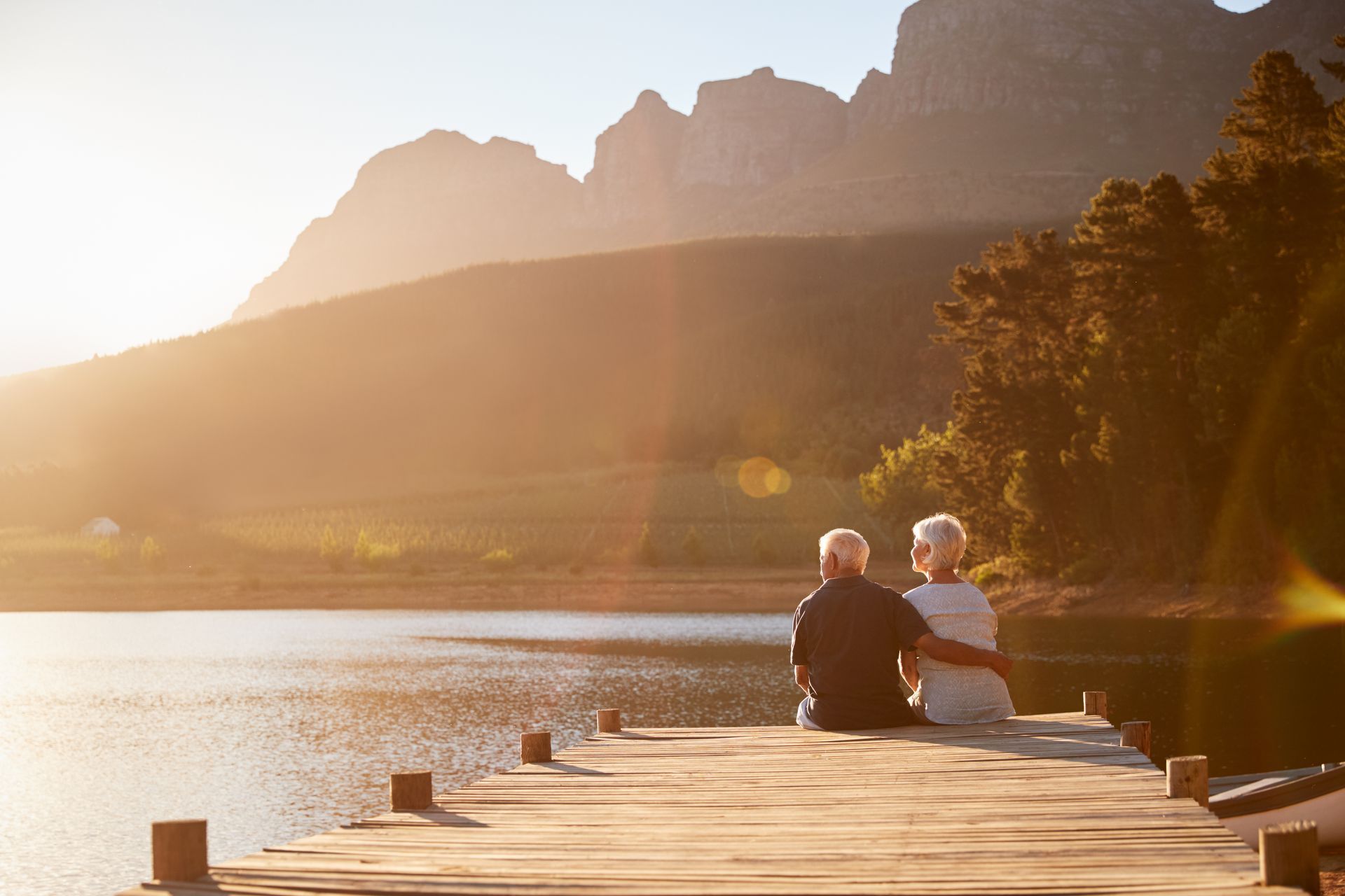 A man and a woman are sitting on a dock overlooking a lake.