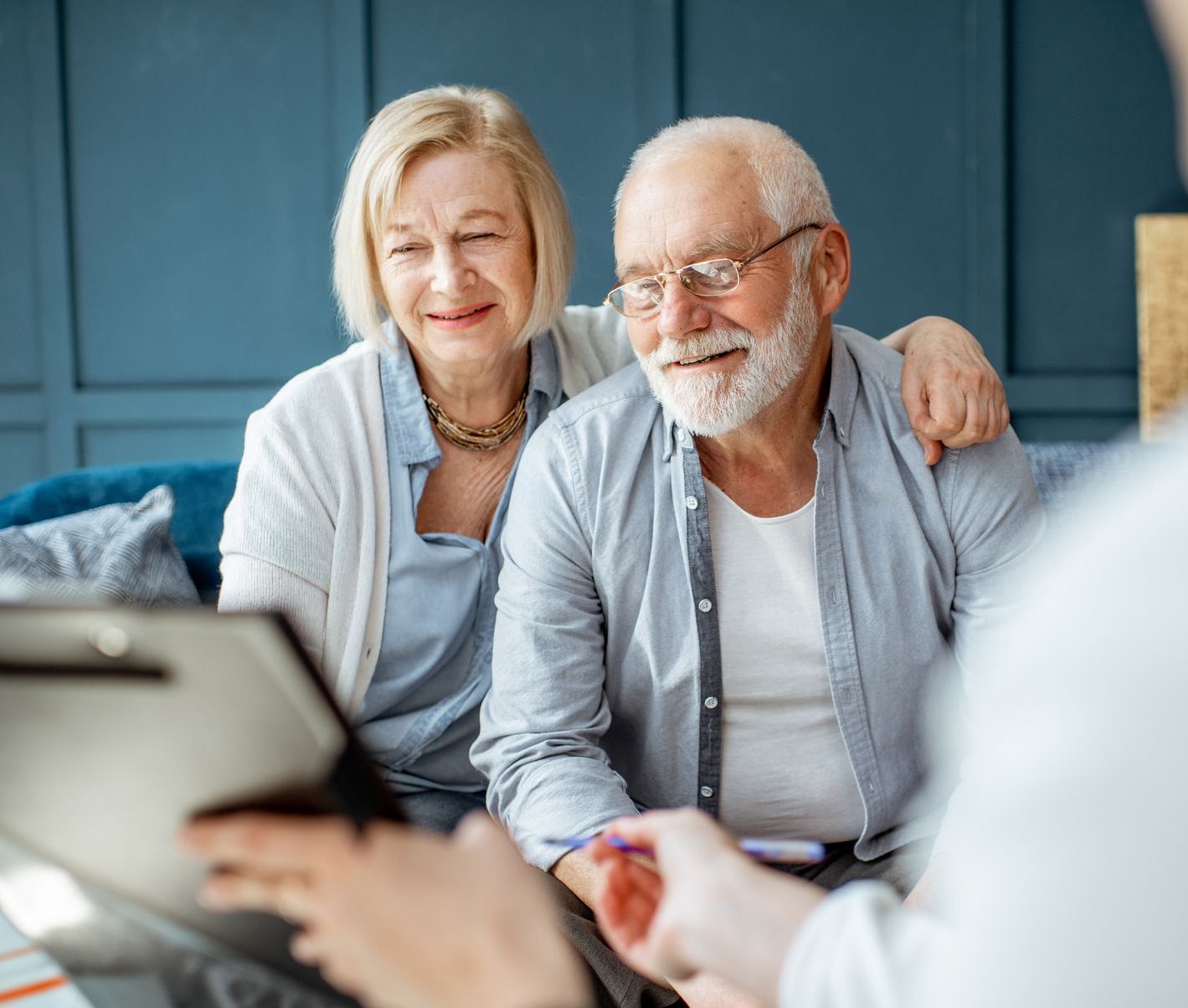 An elderly couple is sitting on a couch talking to a man.