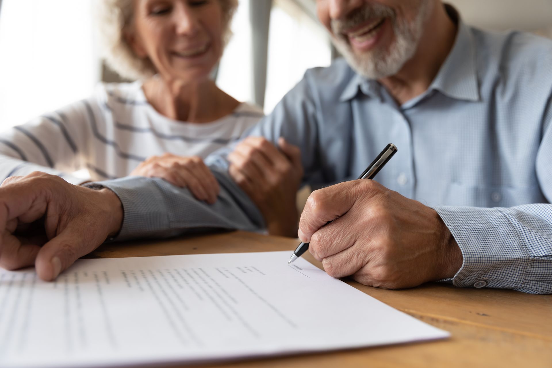 An elderly couple is signing a document at a table.