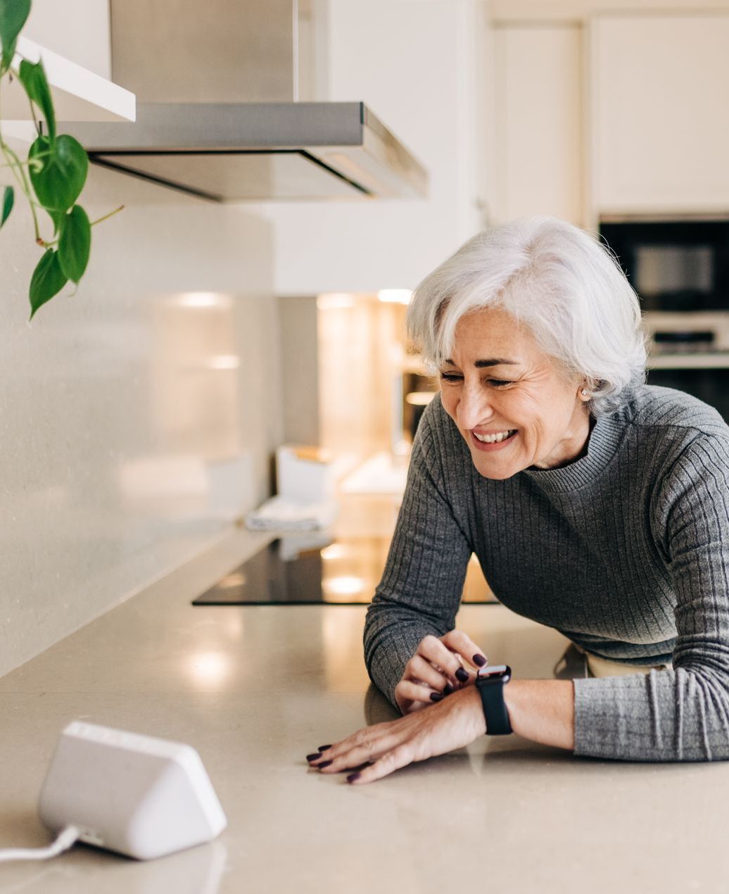 A woman is laying on a kitchen counter looking at her smart watch.