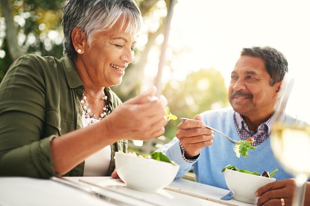 A man and a woman are sitting at a table eating salad.
