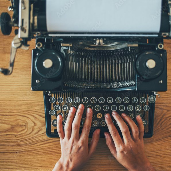 Eine Person tippt auf einer alten Schreibmaschine auf einem Holztisch.