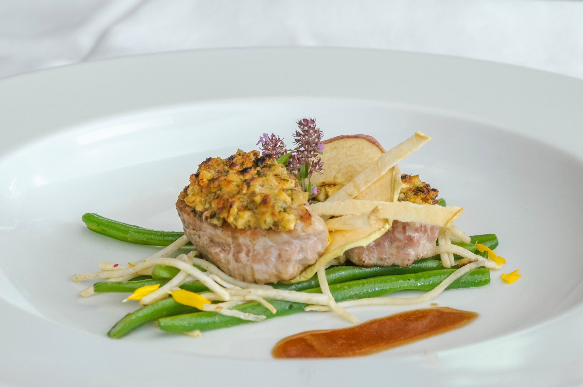 Ein weißer Teller mit Fleisch und grünen Bohnen auf einem Tisch.