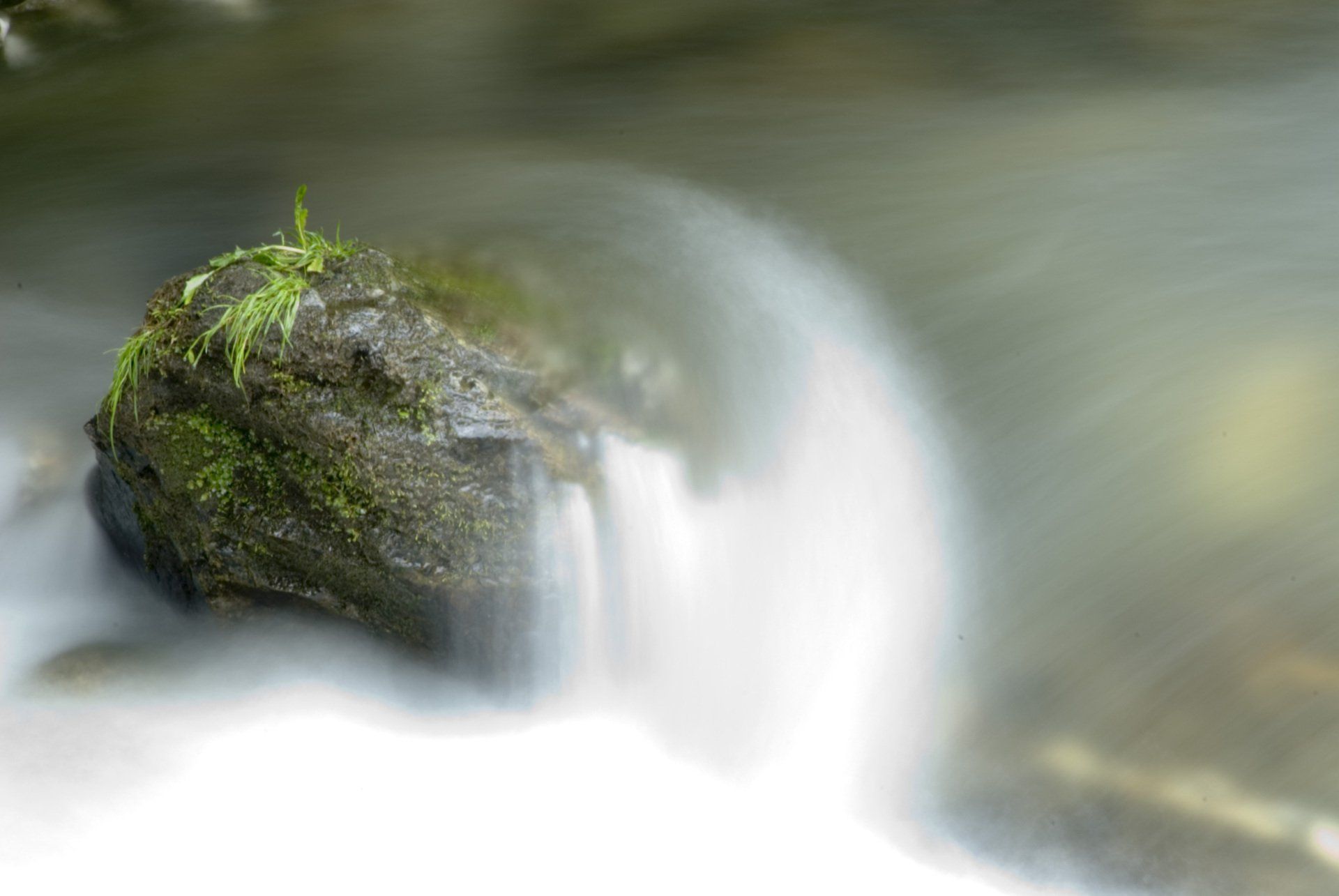 Eine Nahaufnahme eines Wasserfalls mit einem Felsen im Vordergrund.