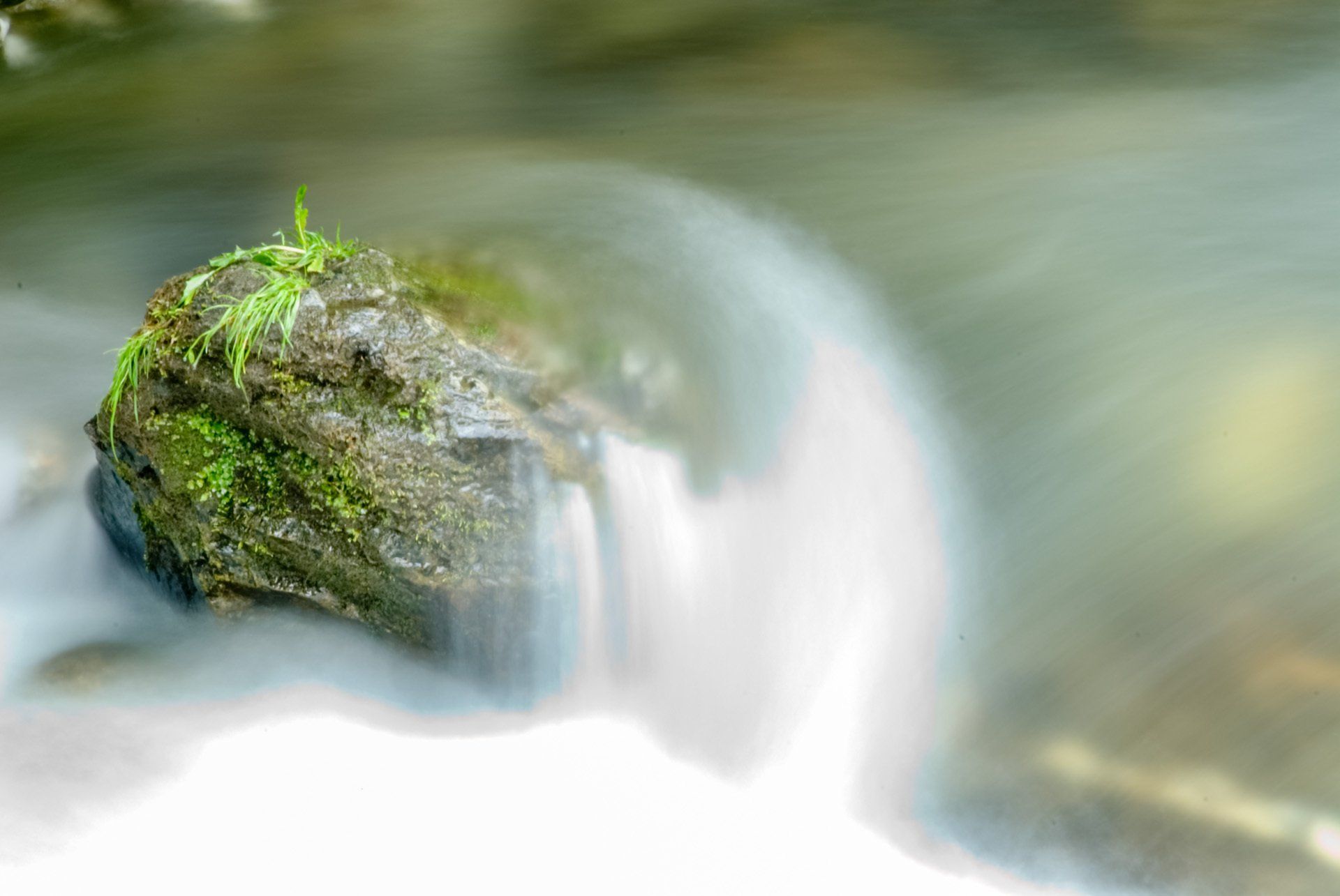 Eine Nahaufnahme eines Wasserfalls mit einem Felsen im Vordergrund.
