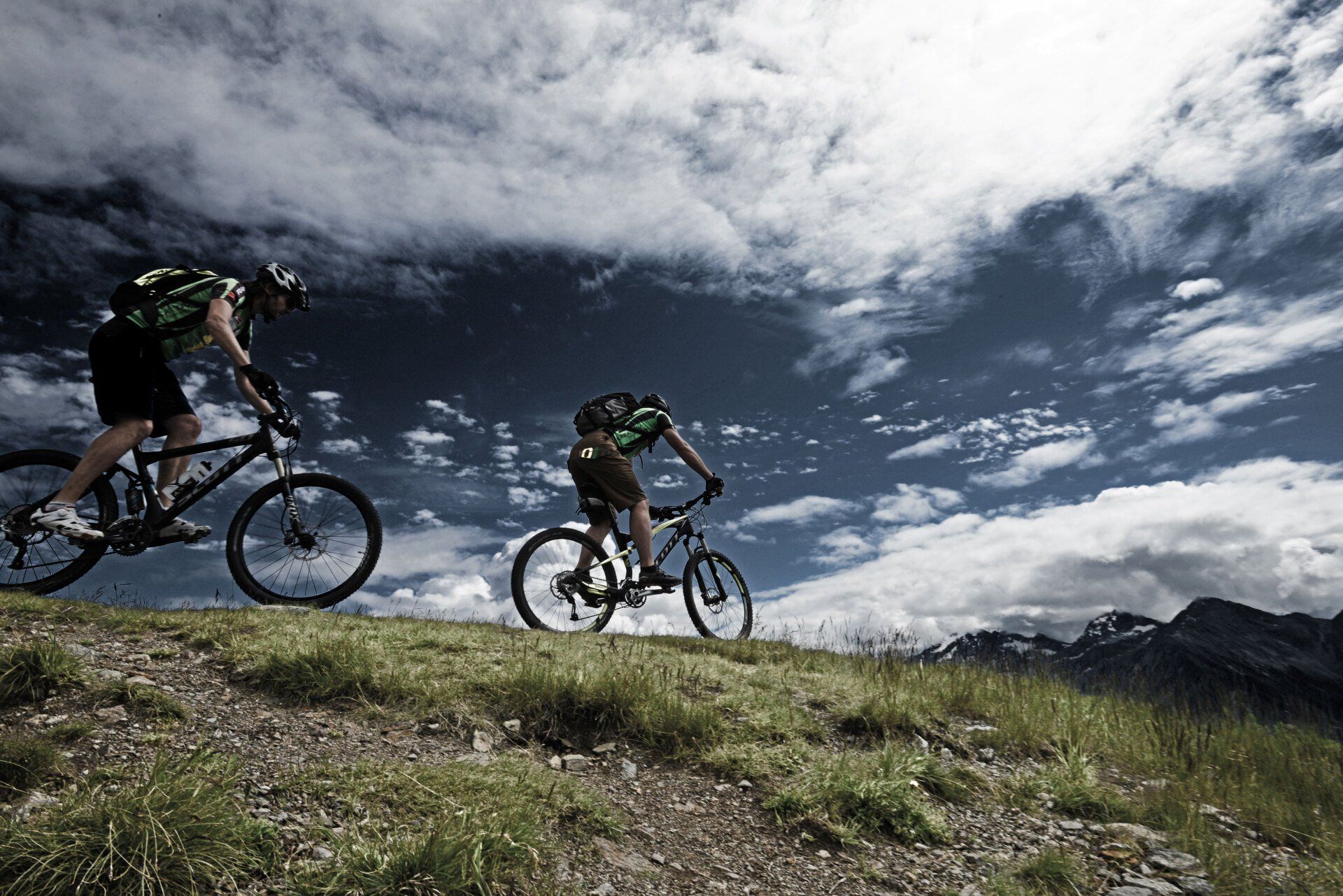 Zwei Personen fahren mit dem Fahrrad einen grasbewachsenen Hügel hinunter.