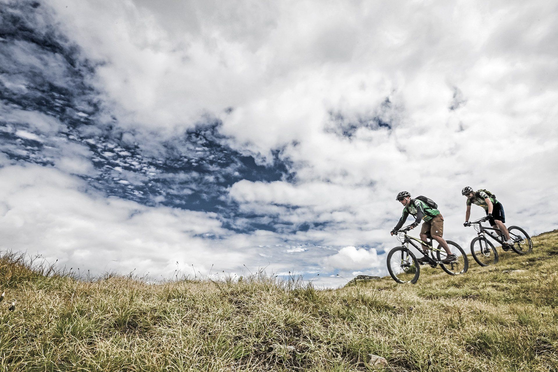 Zwei Personen fahren mit dem Fahrrad einen Hügel hinunter.