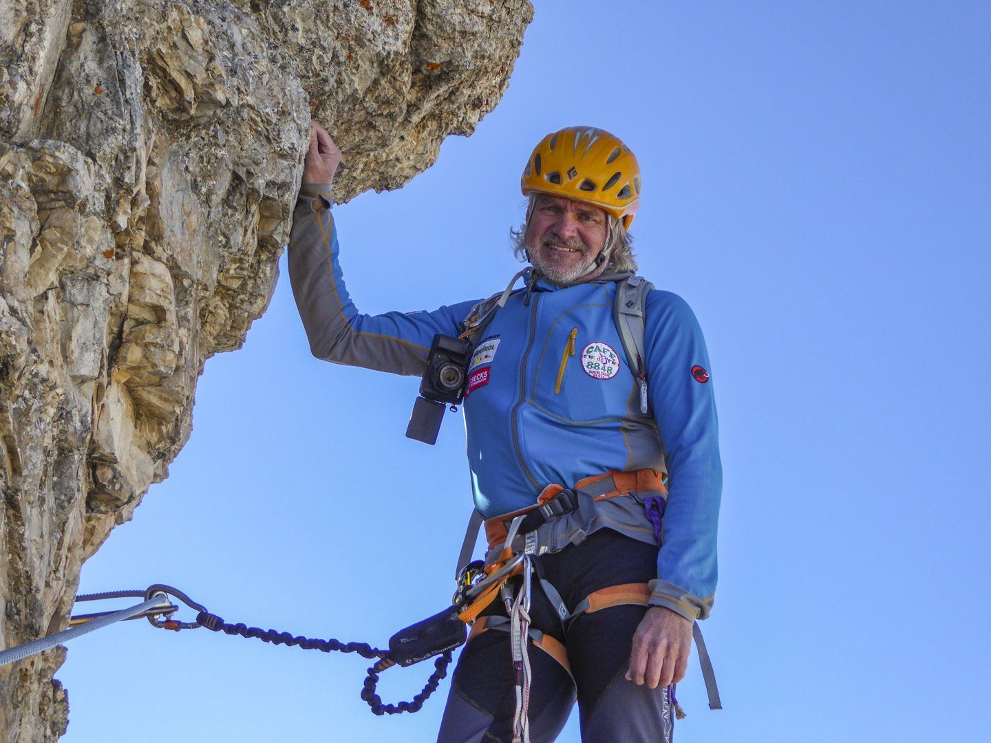 Ein Mann mit einem blauen Hemd und einem gelben Helm klettert eine Felswand hinauf.