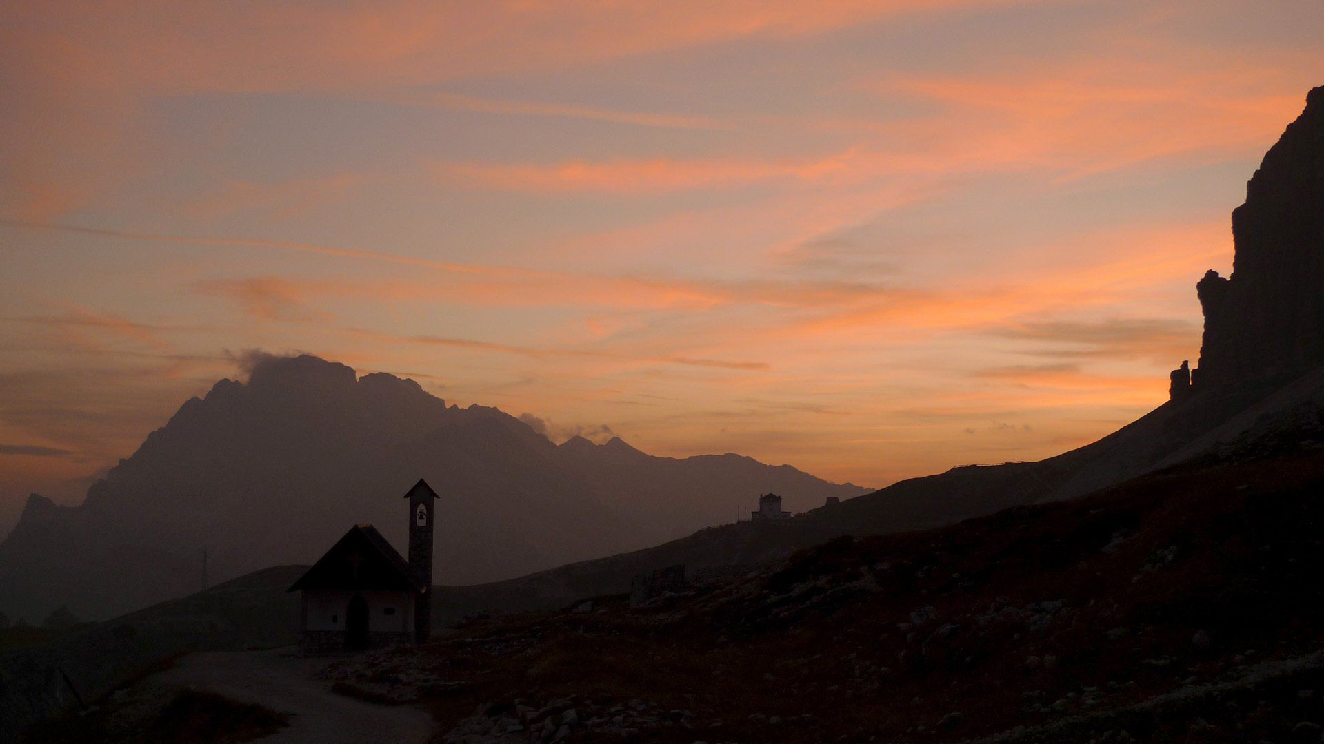 Die Silhouette einer Kirche zeichnet sich vor dem Abendhimmel mit Bergen im Hintergrund ab.