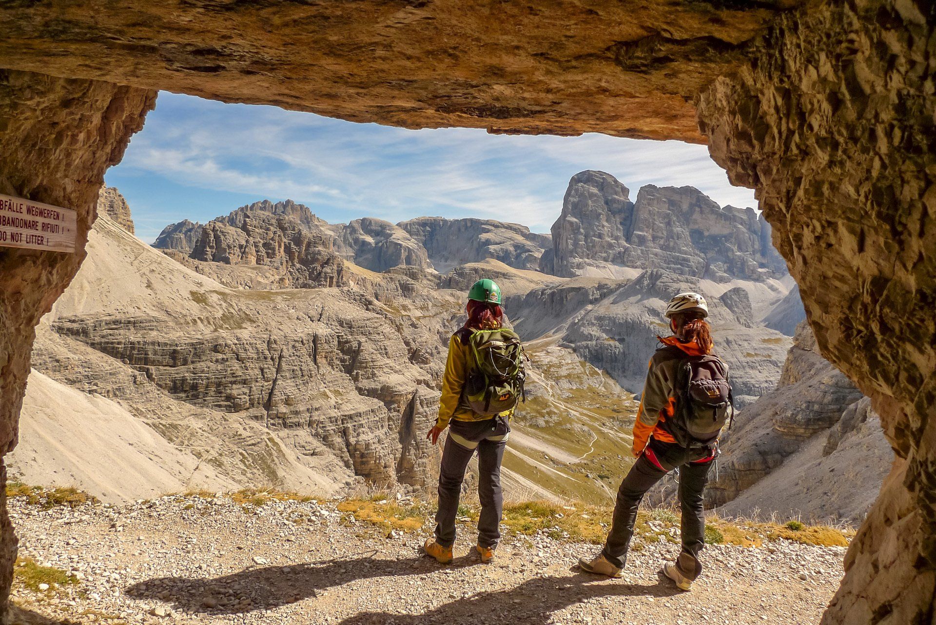 Zwei Menschen stehen in einer Höhle und blicken auf eine Bergkette.
