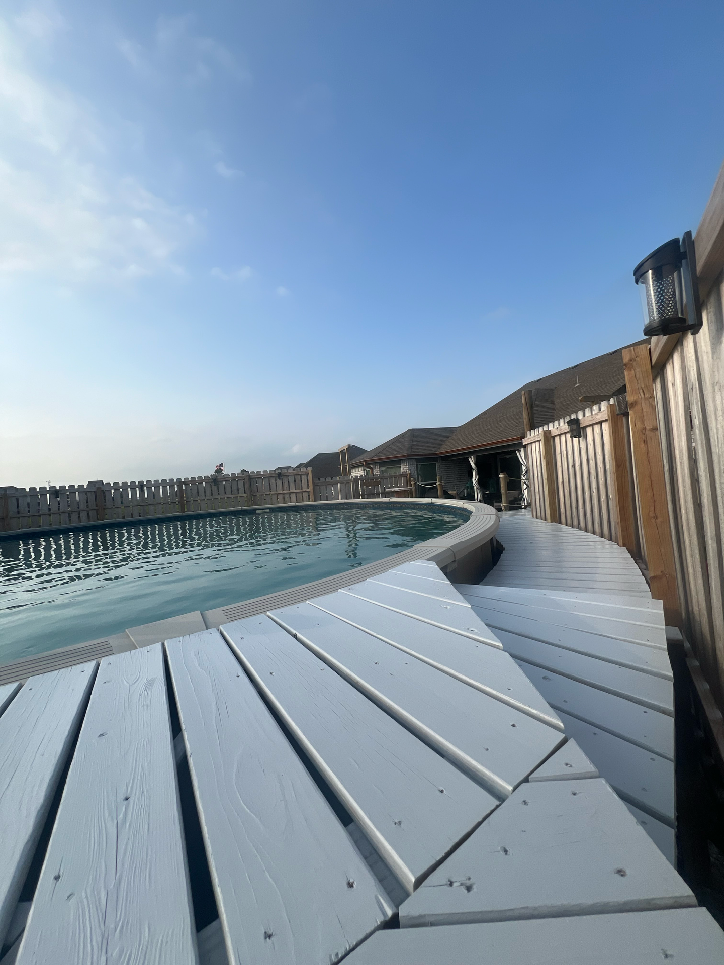 A wooden deck with a swimming pool in the background.