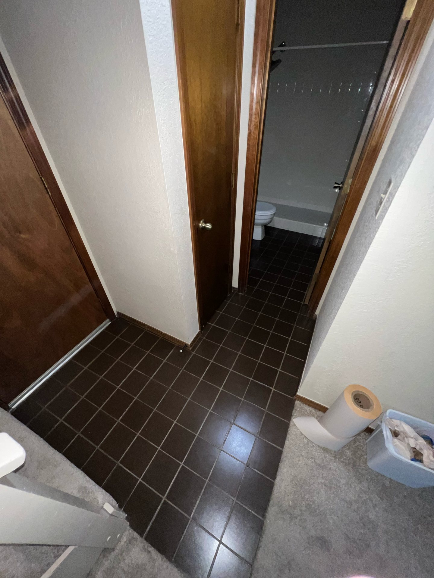 A hallway with brown tile floors leading to a bathroom.