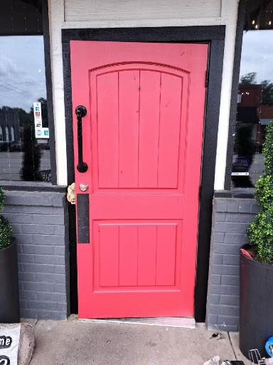 A red door is sitting in front of a brick building.