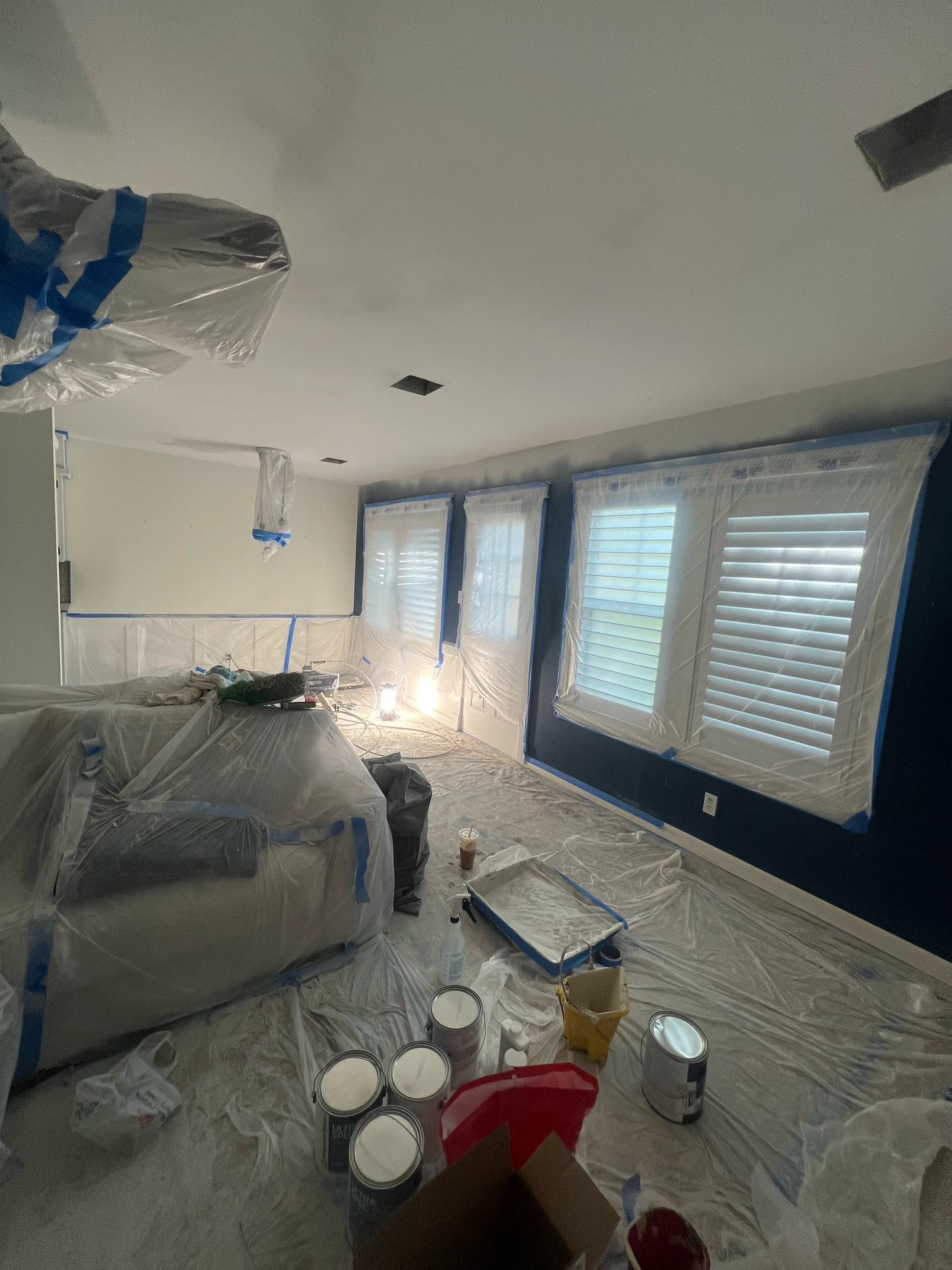 A living room is being painted and covered in plastic.