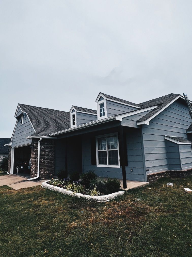 A blue house with a gray roof is sitting on top of a lush green lawn.