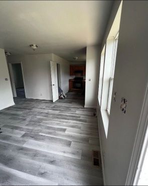 A living room with hardwood floors and a kitchen in the background.